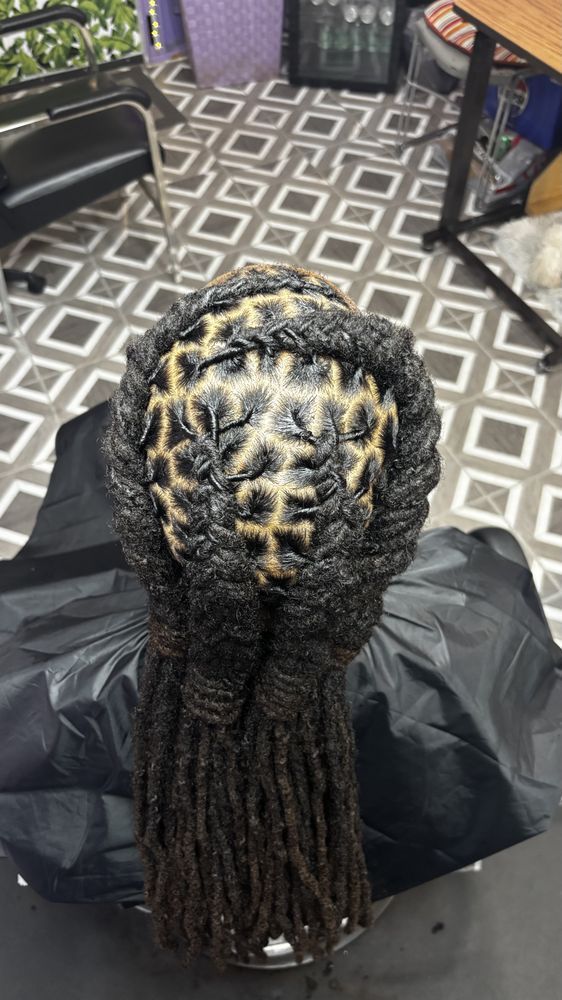 Person with locs, intricately styled with geometric patterns on top, with long hanging locs. Indoors, looking down.