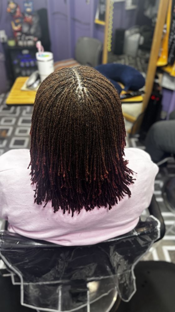 Back view of a person with micro braids, brown with red ends, in a salon chair.