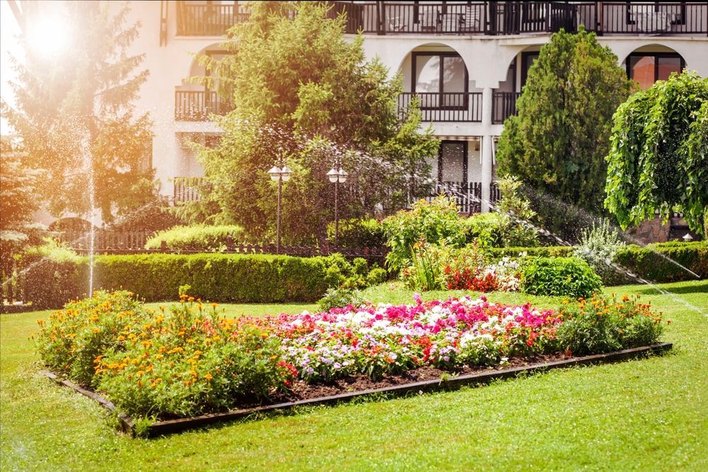 A garden with flowers and sprinklers in front of a building.
