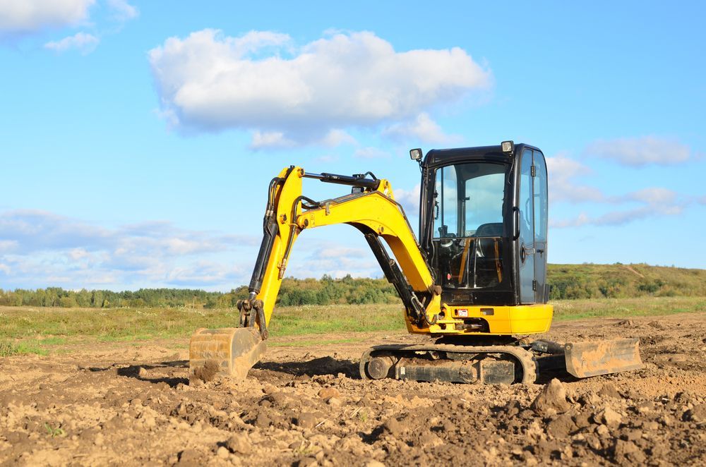 A small yellow excavator is digging a hole in a dirt field.