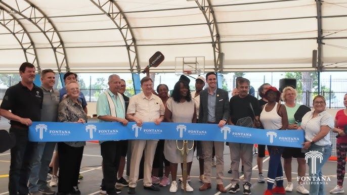 A group of people standing in a row, holding a blue Fontana ribbon during a ribbon-cutting ceremony at an indoor court.