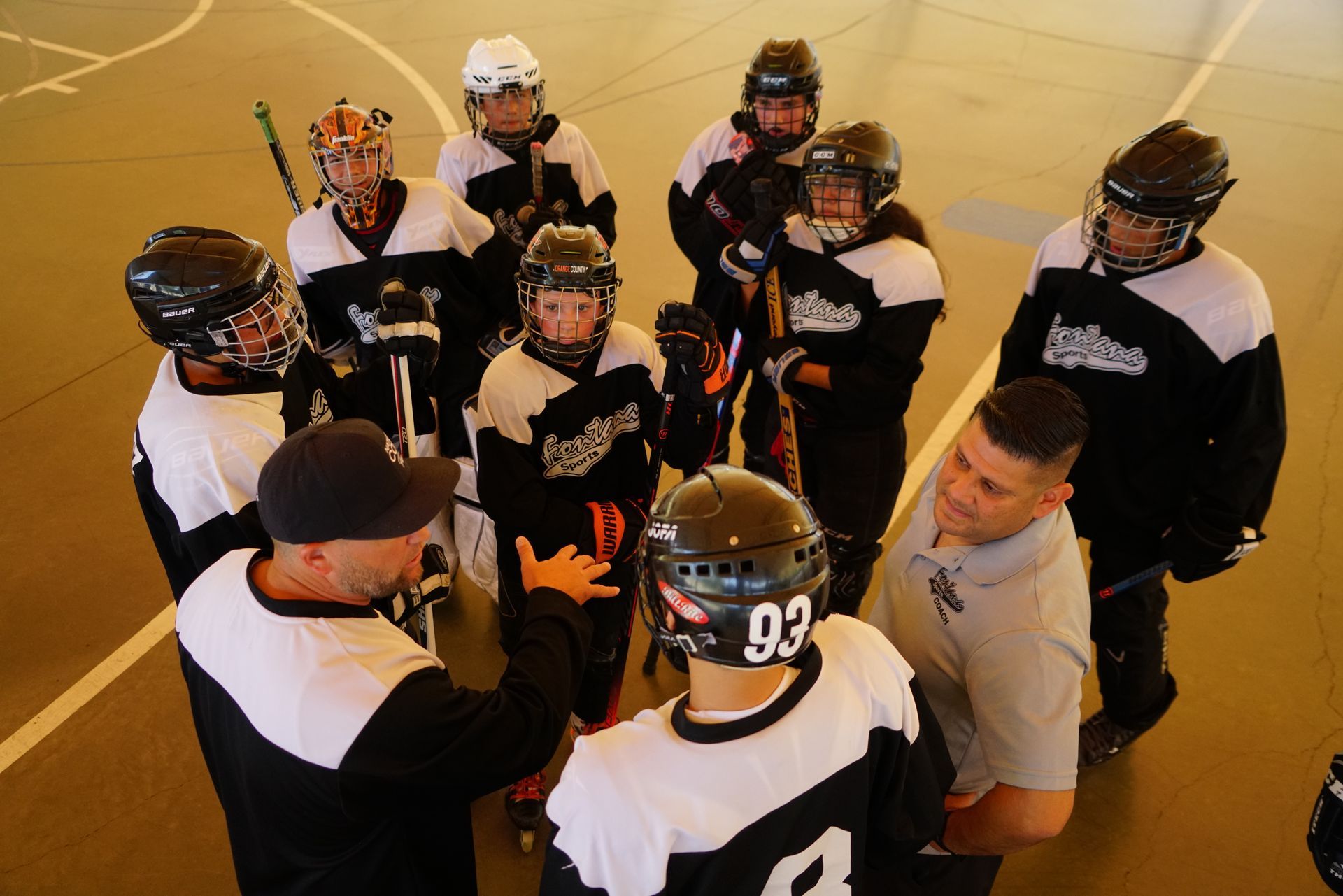 A coach speaks to a group of roller hockey players in matching black and white jerseys during a practice session.
