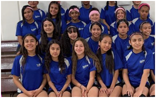 A group of students in matching blue sports jerseys posing for a photo indoors.