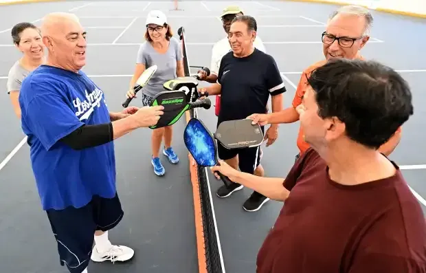 A group of people standing on a pickleball court, smiling and holding their paddles together over the net.