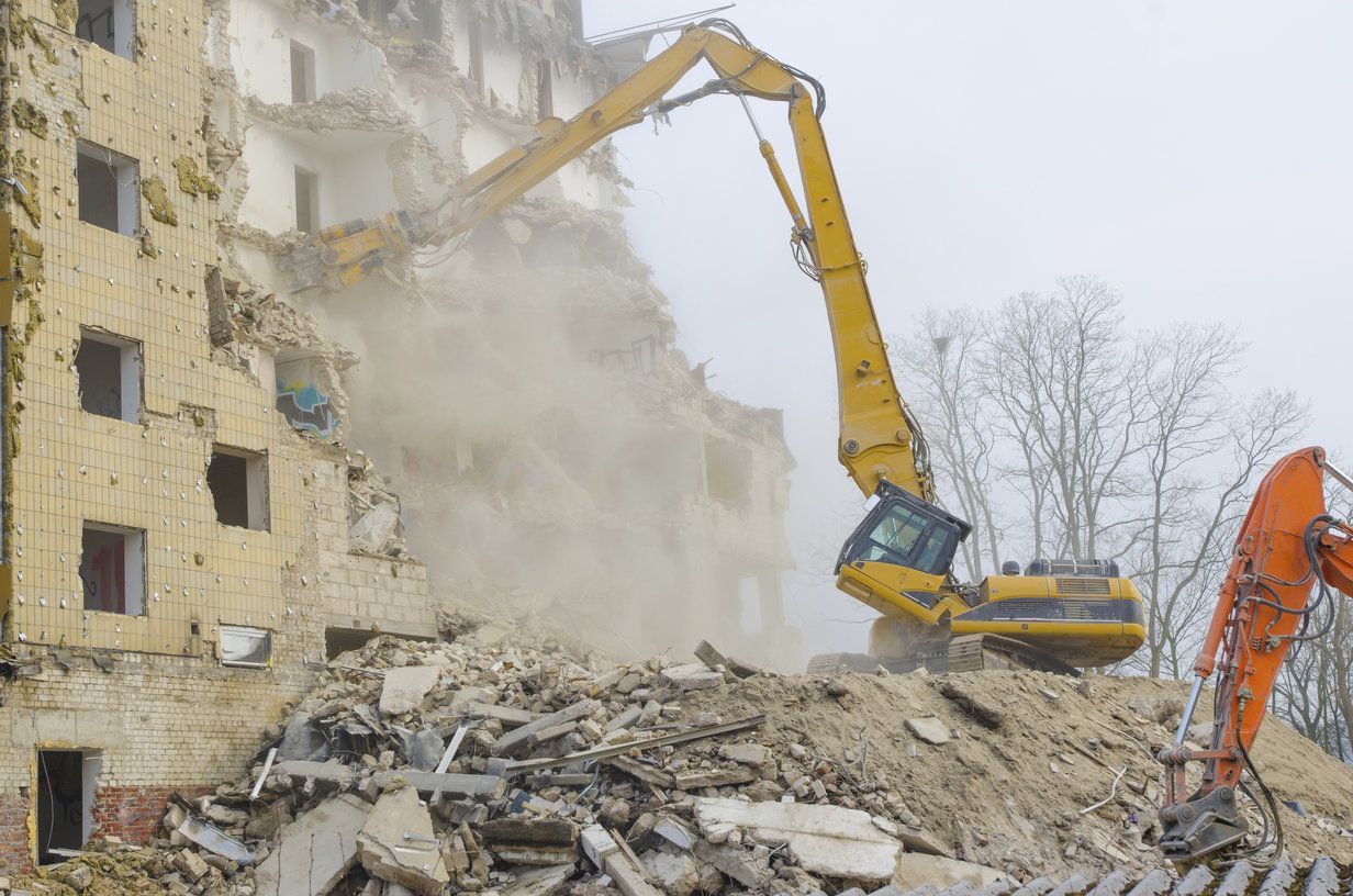 Yellow excavators demolishing a building amid rubble and dust