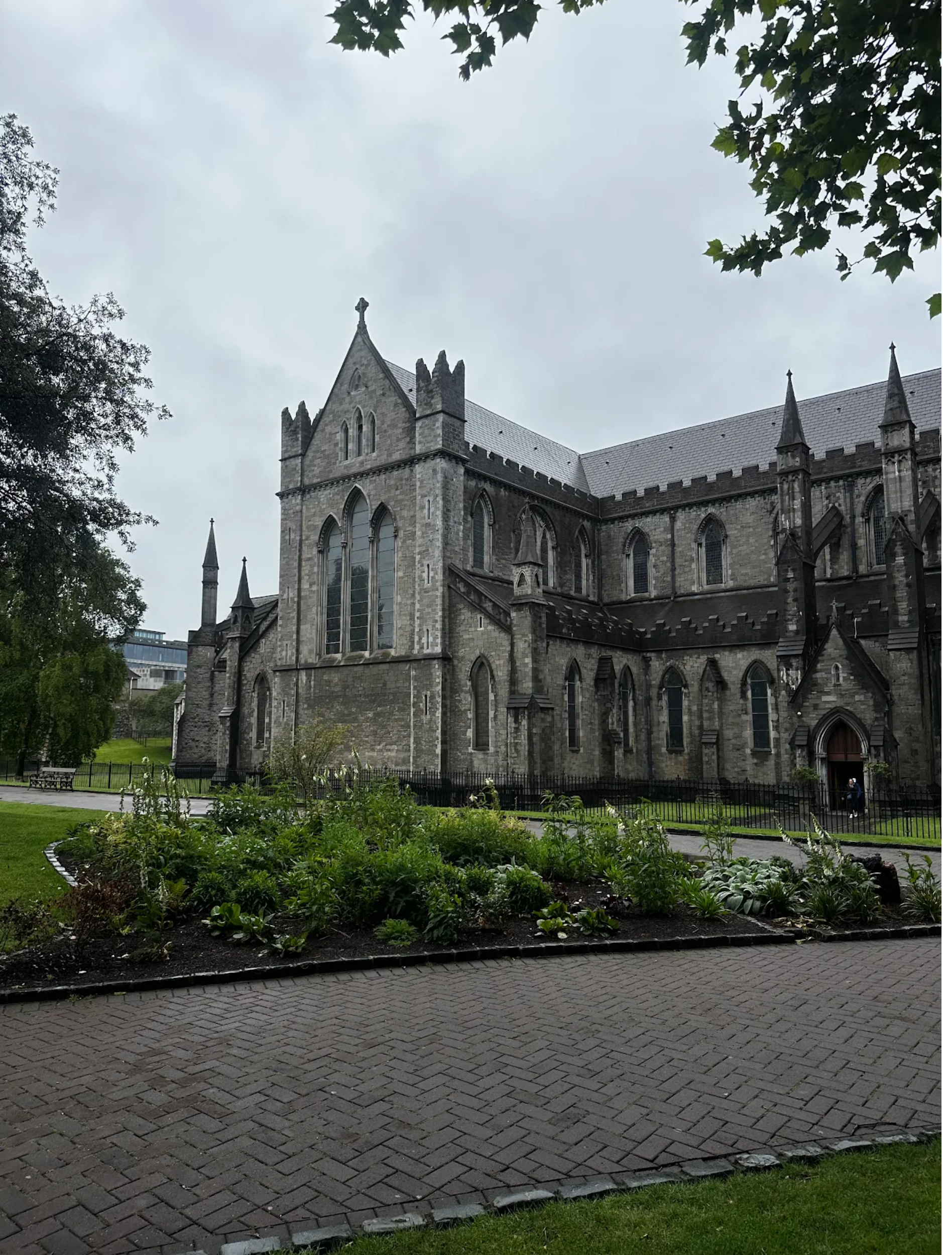 Gothic stone cathedral with tall spires beside a wet garden path under an overcast sky