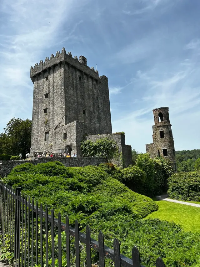 Stone castle tower and ruins behind green hedges under a blue sky