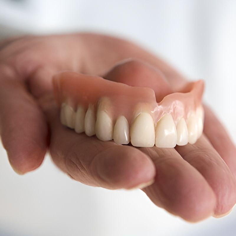 A Person is Holding a Denture in Their Hand — Central Coast Denture Clinic Erina In Erina, NSW