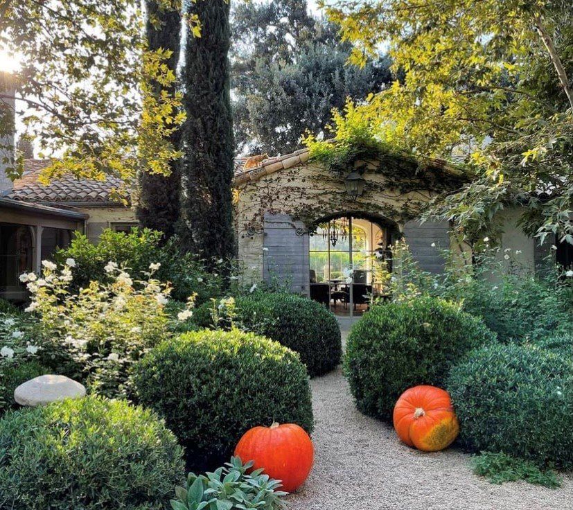 Garden path with two orange pumpkins leading to a stone archway and lush greenery