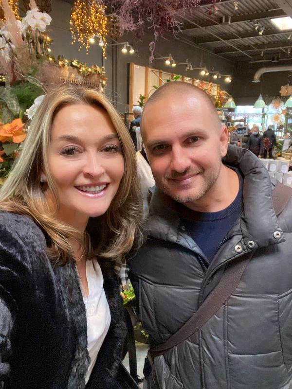 Smiling pair posing indoors in a festive market with warm string lights and decorated stalls