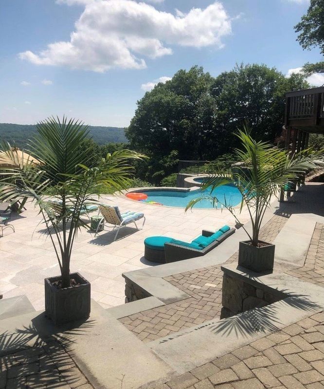 Sunny patio with turquoise pool, palm plants, and lounge chairs overlooking a scenic hillside view