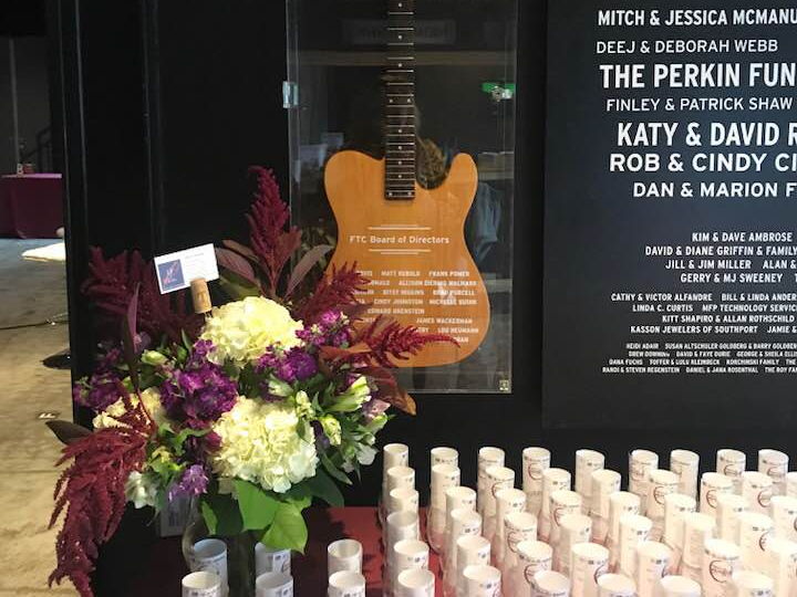 Memorial display with flowers, candles, and a guitar-shaped sign in a dark window memorial.