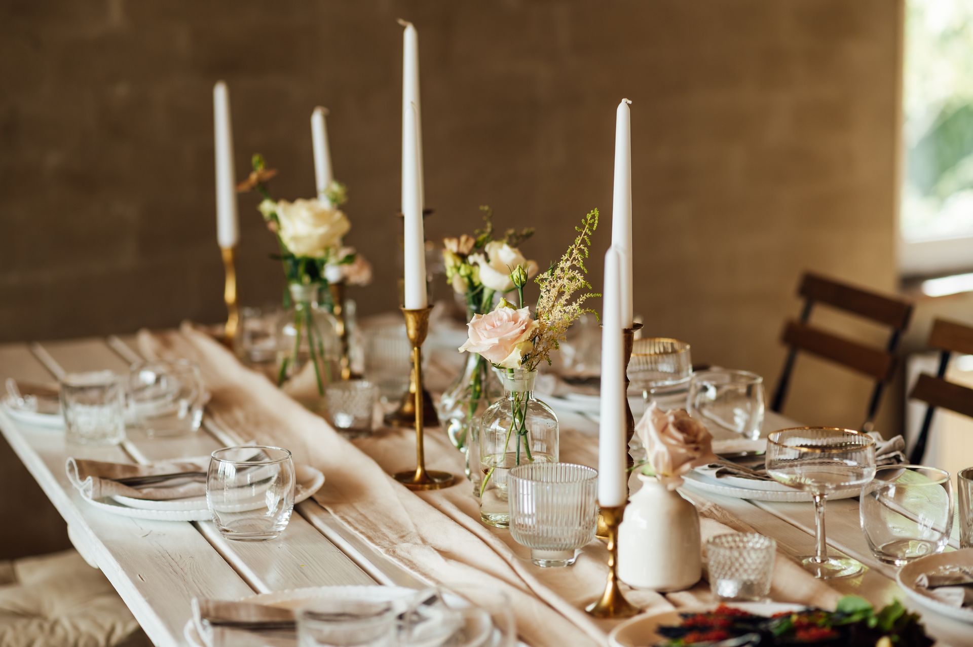 Rustic dining table set with white candles, flowers, glassware, and table settings for an elegant meal Rustic dining table set with white candles, flowers, glassware, and table settings for an elegant meal