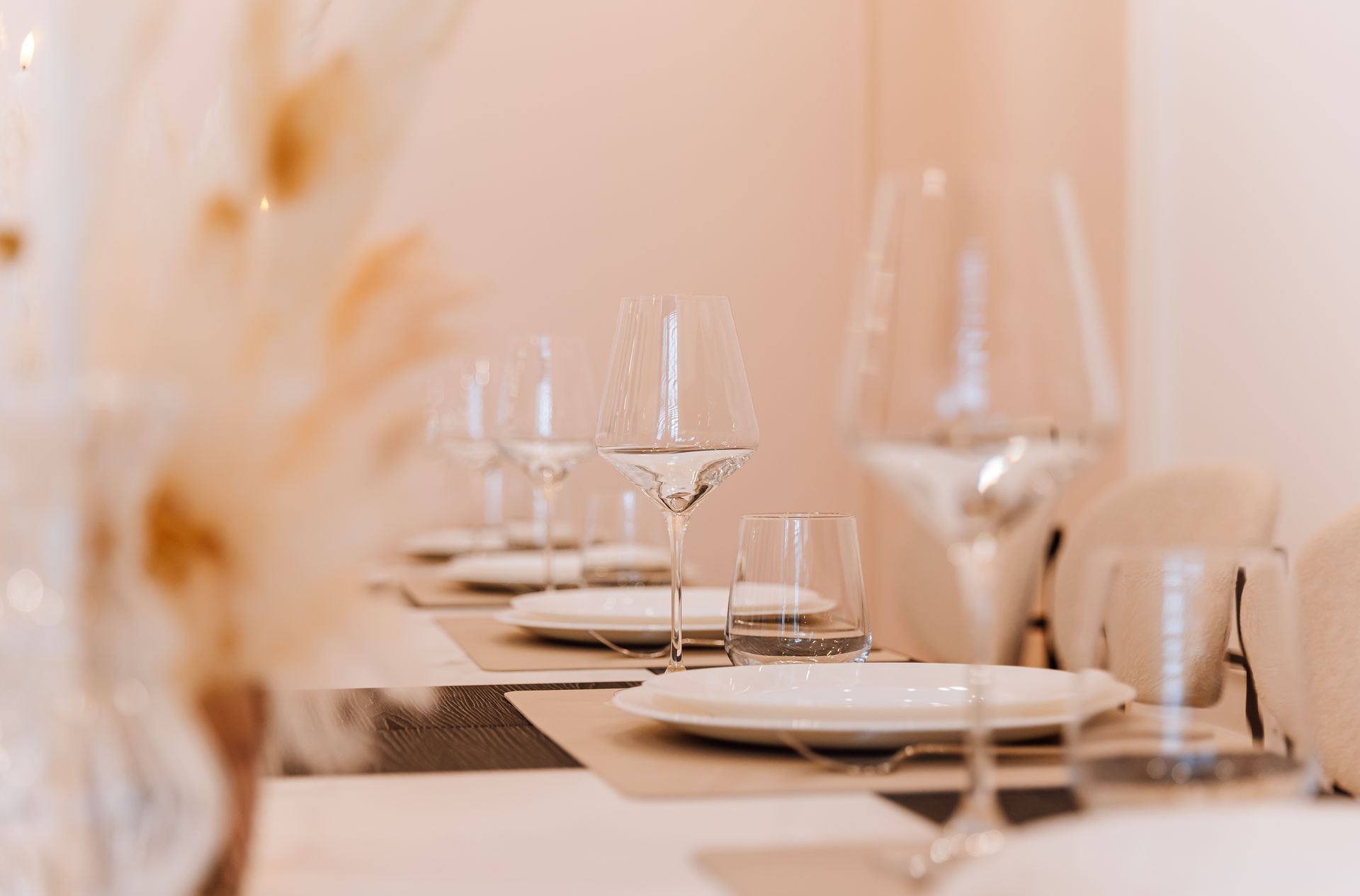Elegant dining table set with white plates, wine glasses, and beige decor in a softly lit restaurant Elegant dining table set with white plates, wine glasses, and beige decor in a softly lit restaurant