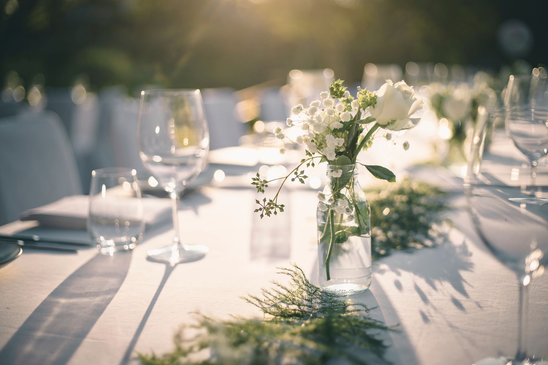 Elegant outdoor dining table with white flowers, glassware, and sunlight Elegant outdoor dining table with white flowers, glassware, and sunlight