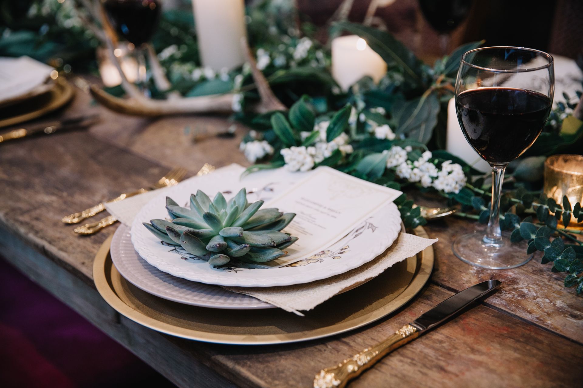 Elegant dinner table set with white plates, green succulent centerpiece, candles, and wine glasses Elegant dinner table set with white plates, green succulent centerpiece, candles, and wine glasses