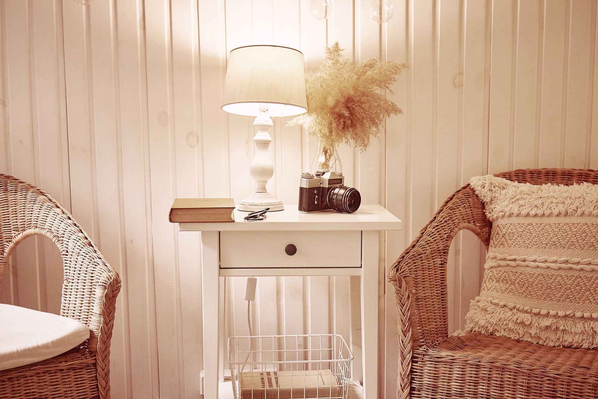 Cozy cream living room with wicker chairs, side table, lamp, and dried flowers