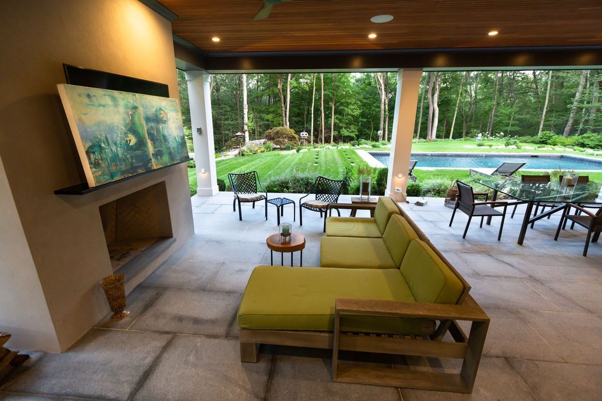 Modern patio with green sofa, dining tables, and a fire pit overlooking lush tropical garden