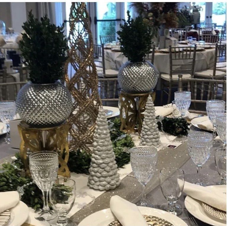 Elegant banquet table with silver decor, white napkins, glassware, and tall centerpieces in a bright event hall