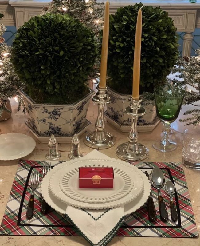 Elegant holiday table setting with plaid placemats, candles, greenery, and a red gift box centerpiece