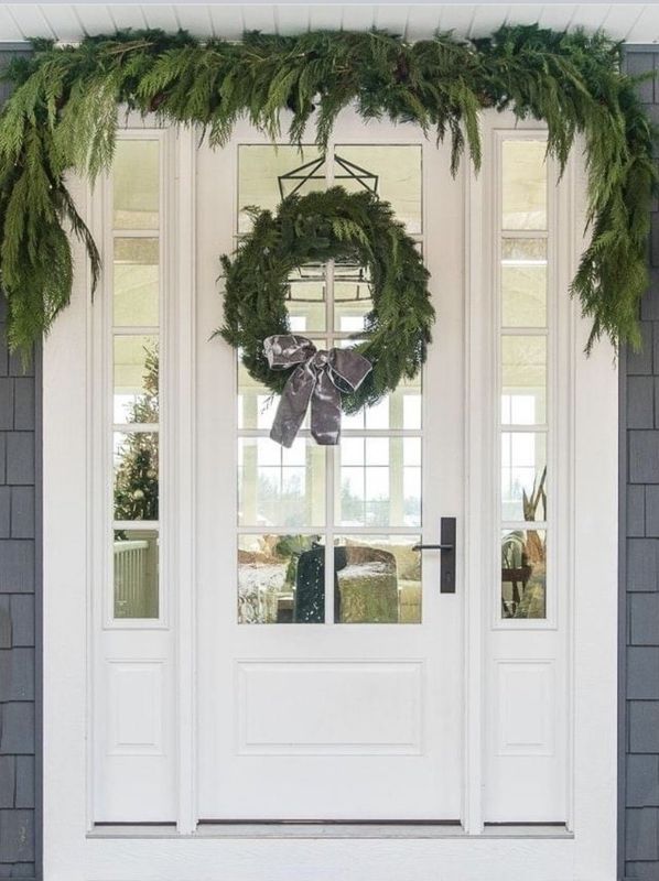 Front porch with white double doors, glass sidelights, and green holiday wreath and garland decor.
