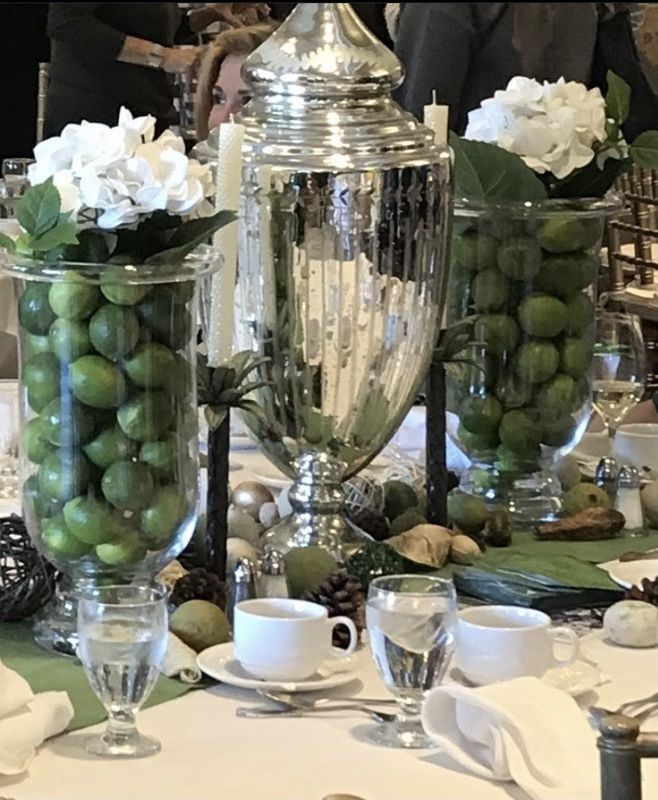 Elegant table centerpiece with silver vase and green limes in glass, surrounded by white flowers and place settings