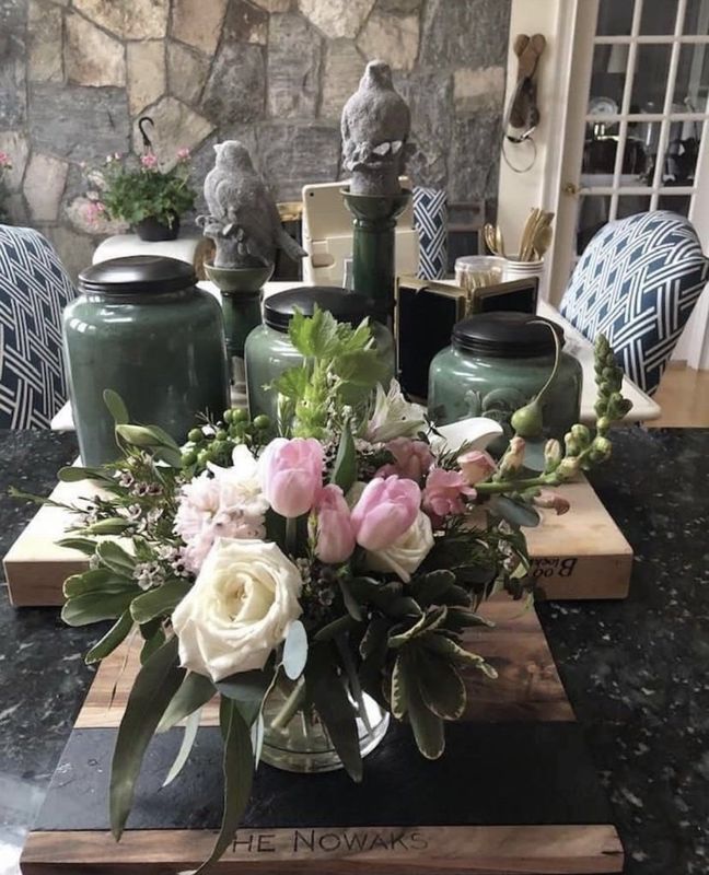 Green jars and pink-white flowers arranged as a floral centerpiece on a rustic table outdoors