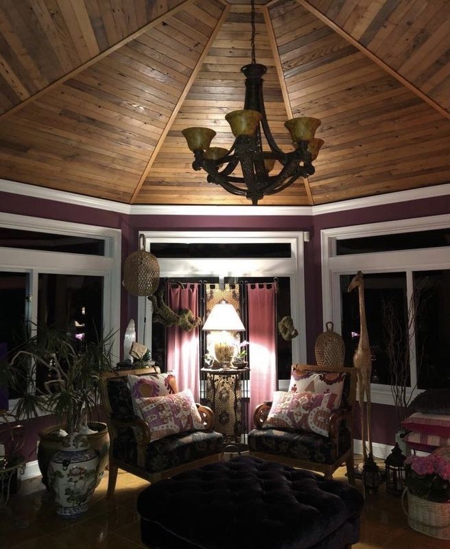 Cozy octagonal sunroom with wood ceiling, chandelier, windows, patterned chairs, and soft lamp light