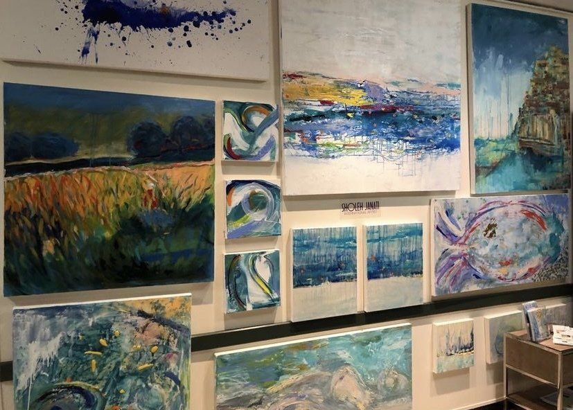 Art gallery wall with colorful landscape paintings and abstract blue-and-green canvases.