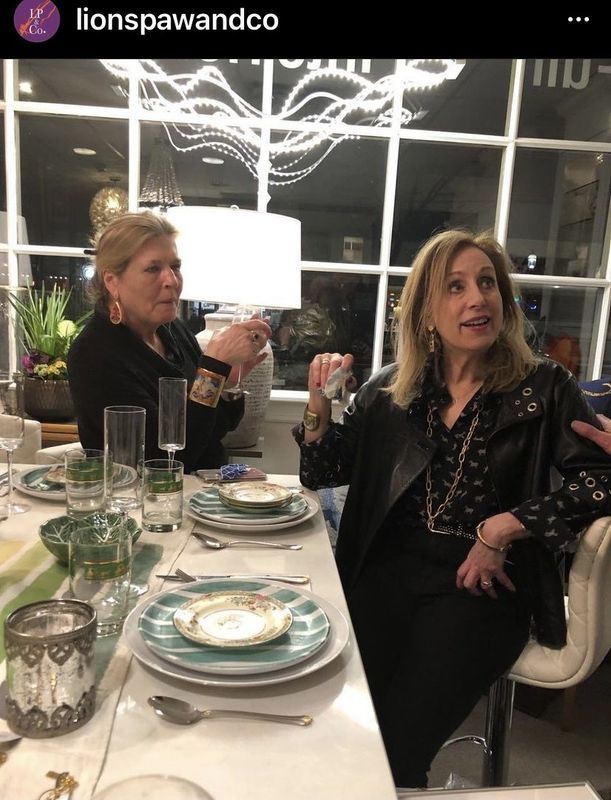 Two women seated at a restaurant table, chatting over a meal with drinks and plates in front of them.