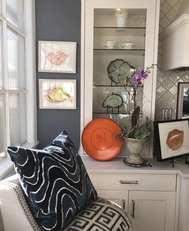 Decorative shelves with dishes, art, orchids, and an orange tray above patterned pillows