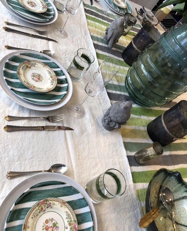 Elegant table setting with striped plates, silverware, and green glassware on a striped tablecloth