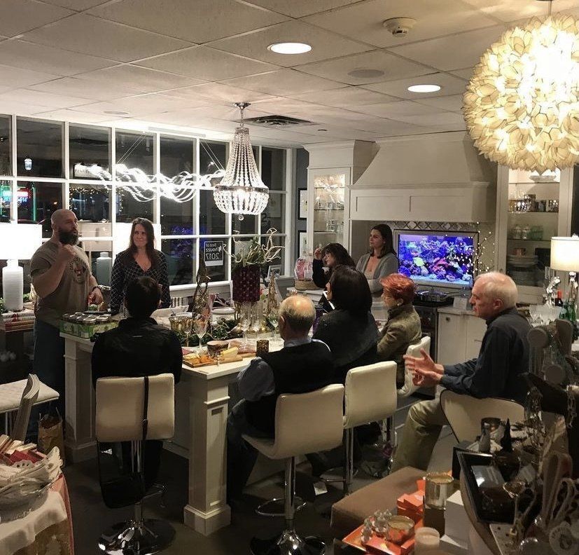 Guests seated around a dining table in a bright, modern room with chandeliers and a decorated window