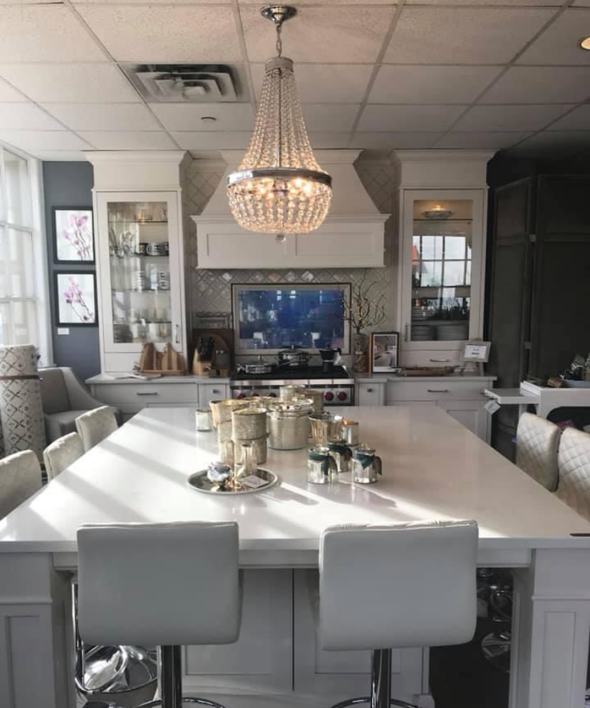 Elegant kitchen with a large white island, crystal chandelier, and built-in cabinetry under bright natural light