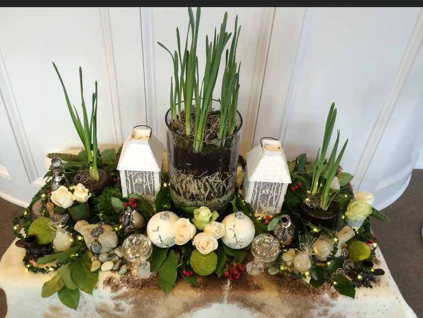 Floral tabletop centerpiece with white flowers, greenery, candles, and lanterns in a glass vase arrangement