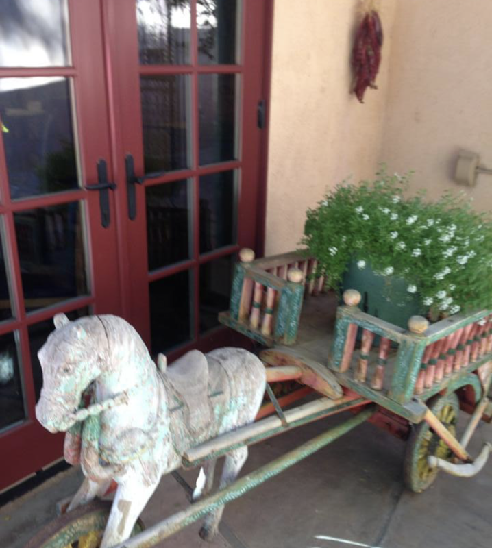 White horse-drawn cart with flower planters parked by a red door and wall