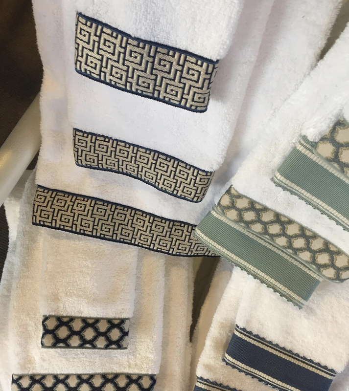Close-up of white towels with patterned woven borders in beige, green, and navy accents