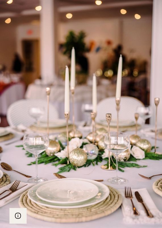 Elegant white and gold banquet table setting with candles, glassware, and floral greenery centerpiece