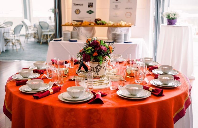 Round banquet table set with red tablecloth, white dishes, and floral centerpiece in a bright dining room Round banquet table set with red tablecloth, white dishes, and floral centerpiece in a bright dining room