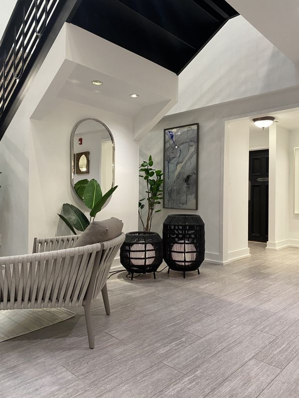 Modern white patio with woven chairs, potted plants, and black accent tables under a vaulted ceiling