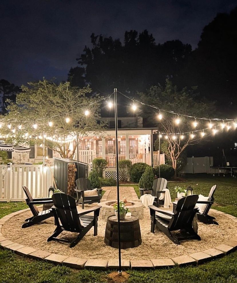Backyard fire pit area with black chairs, string lights, and a house at night Backyard fire pit area with black chairs, string lights, and a house at night