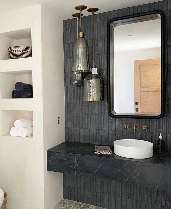 Modern bathroom vanity with black countertop, round sink, mirror, and built-in towel shelves.