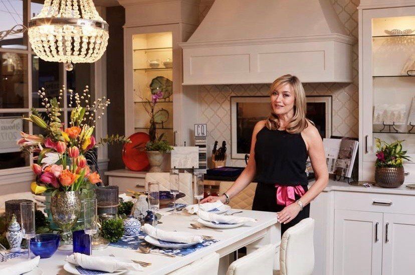Woman standing in a bright kitchen with a set dining table and colorful flowers
