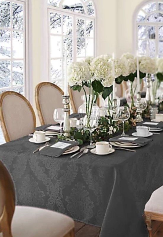 Elegant dining table set with dark tablecloth, white dishes, and tall white floral centerpieces in a bright room