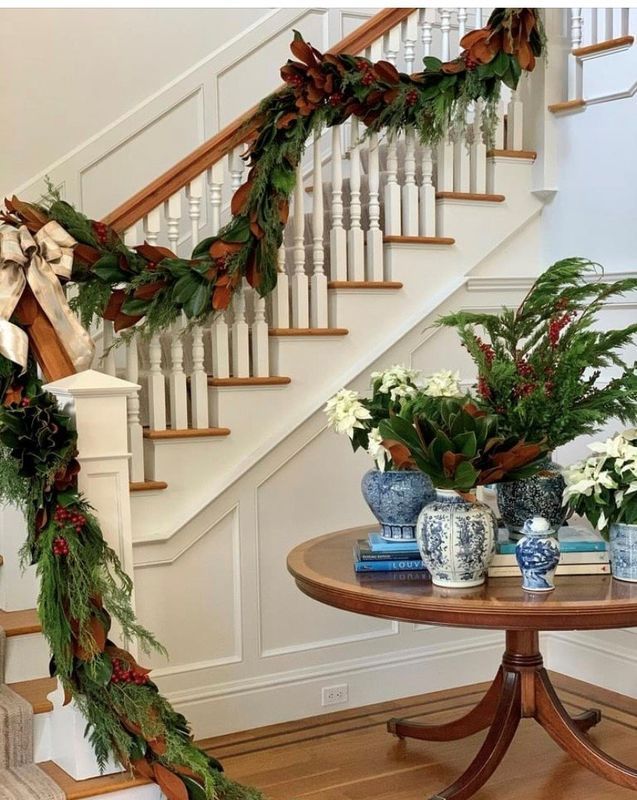 Festive staircase with garland and poinsettias beside a round table of blue-and-white decor