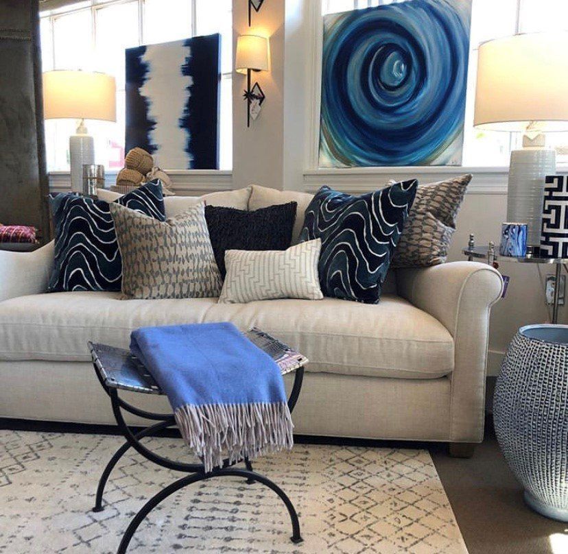 Modern living room with beige sofa, blue patterned pillows, abstract wall art, and a blue throw on a coffee table. Modern living room with beige sofa, blue patterned pillows, abstract wall art, and a blue throw on a coffee table.