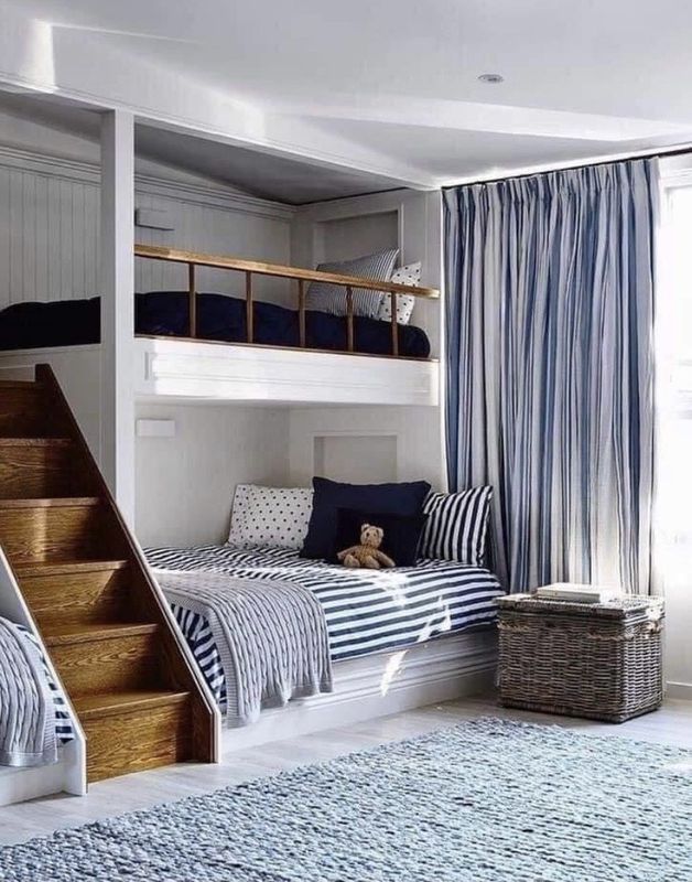 Loft-style twin bedroom with striped bedding, blue curtains, staircase, and woven basket.