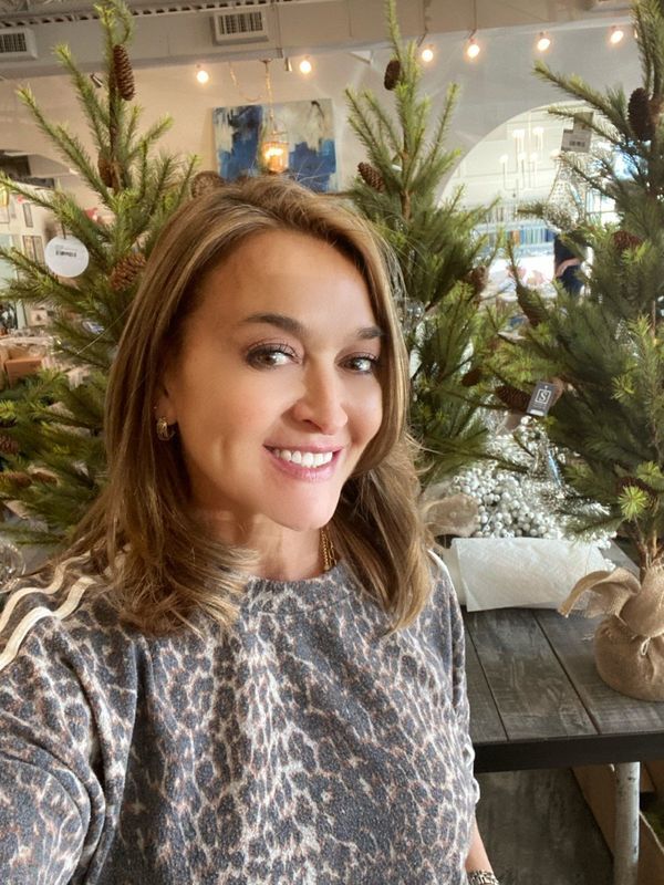 Smiling woman seated by a decorated Christmas tree in a cozy indoor café