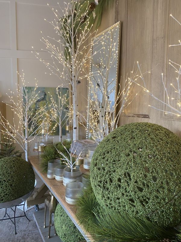 Decorative display with green moss spheres, twinkling branches, and mirrors on a console table