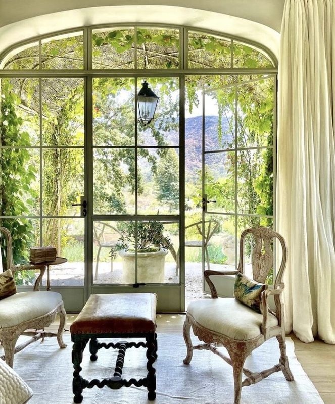 Elegant sunlit sitting room with arched glass doors, cream chairs, and garden views